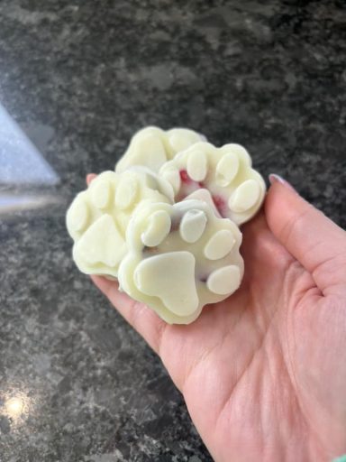 A hand holding several white paw-shaped soap bars.